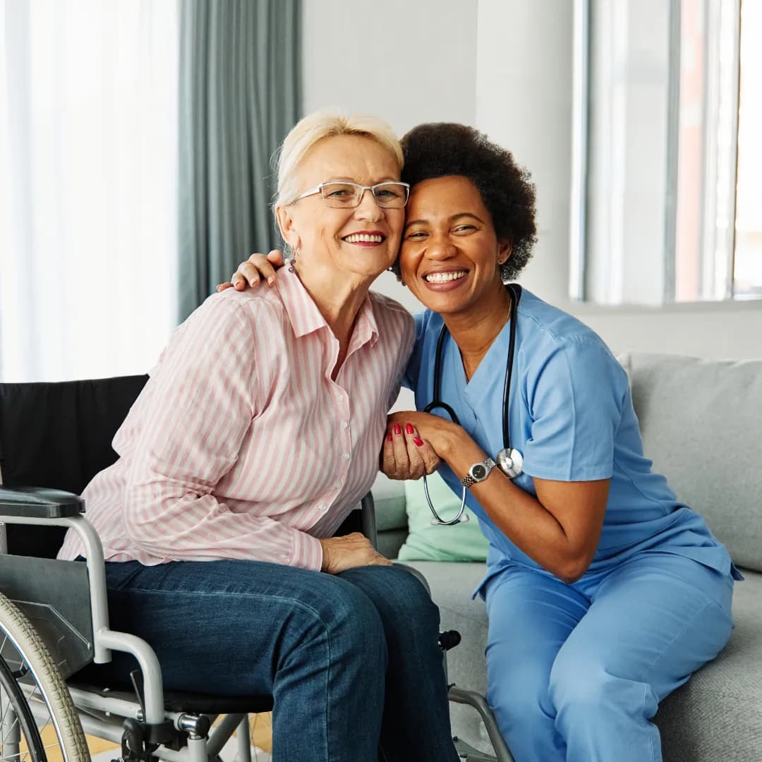 A caregiver hugging a smiling senior woman who uses a wheelchair